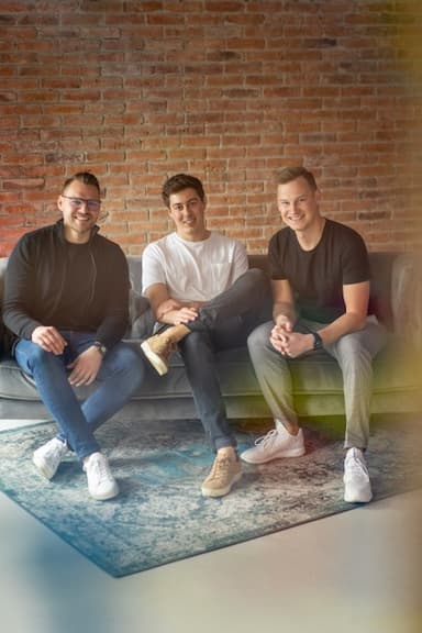 Three members of the aclipp leadership team sitting on a sofa in front of a brick wall, smiling.
