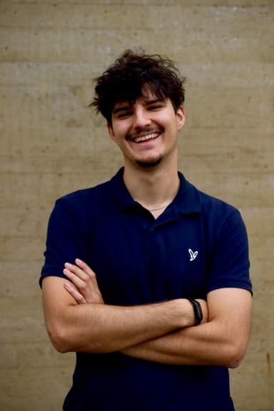Portrait of a smiling team member with folded arms in front of a concrete wall.