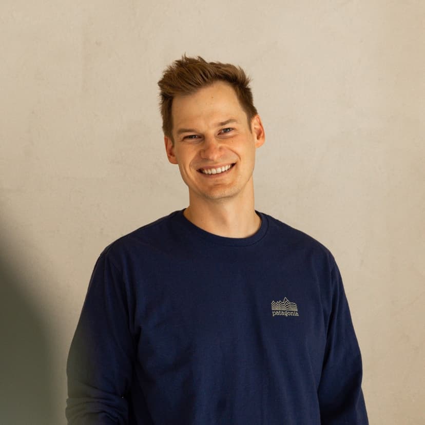 Sascha Kirstein in a portrait, laughing, in front of a light wall.